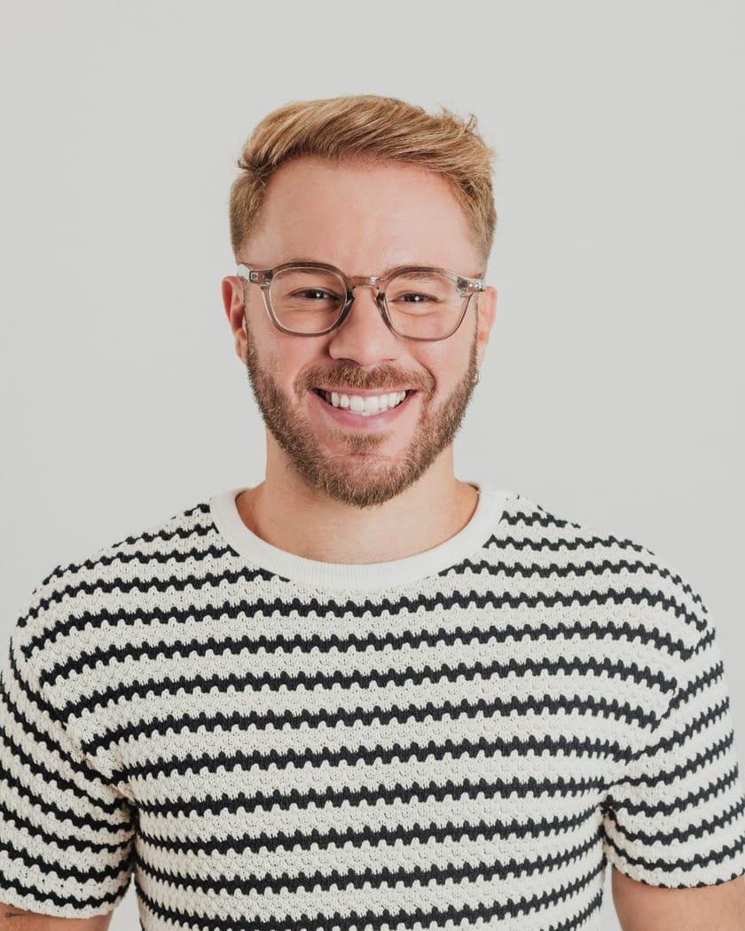 Rafael Figueiredo sorrindo, de óculos e camiseta listrada, em fundo claro